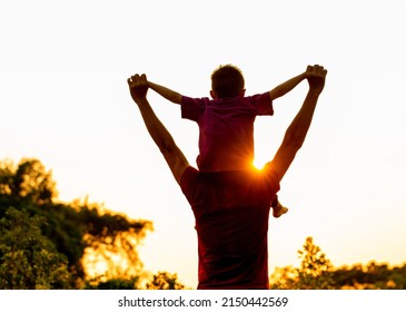 son sitting on father's shoulders in Summer in nature at Beautiful Sunset, silhouette image
