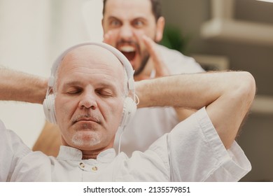 Son yelling at his father who is listening to music on stereo headphones oblivious to his presence - Shutterstock ID 2135579851
