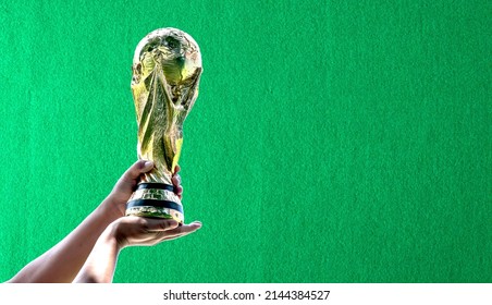 Songkhla, Hat Yai, Thailand 9 Apr 2022: Qatar, World Cup 2022 with green frieze background. hand holding a World Cup winner trophy. The concept for World Cup in Qatar. Copy space on right for a design