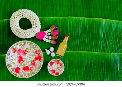 Songkran festival background with jasmine garland, flowers in water bowls, scented water and marly limestone for blessing on wet banana leaf background.