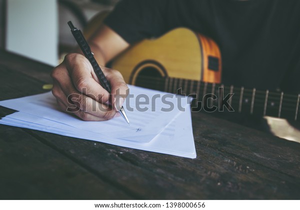 songwriter artist thinking writing\
notes,lyrics in book at studio.man playing live acoustic\
guitar.concept for musician creative.artist composer in work\
process.people relaxing time with\
instrument