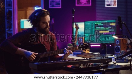 Songwriter musician playing guitar and electronic piano keyboard in home studio, recording acoustics with monitors mixing gear to produce new modern songs. Equalizer and daw software. Camera A.