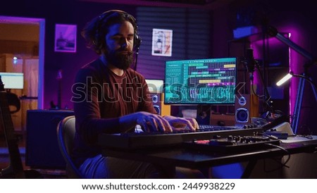 Songwriter musician playing guitar and electronic piano keyboard in home studio, recording acoustics with monitors mixing gear to produce new modern songs. Equalizer and daw software. Camera B.