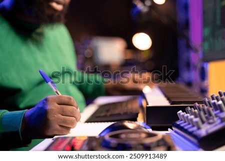 Songwriter taking notes to create new tracks for an album in his home studio, writing lyrics and harmonic elements before recording his song and editing on software, acoustical engineering.
