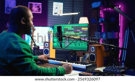 Songwriter taking notes to create new tracks for an album in his home studio, writing lyrics and harmonic elements before recording his song and editing on software, acoustical engineering. Camera B.