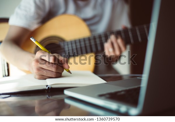 songwriter thinking and writing notes,lyrics\
in book at studio.man playing live acoustic guitar.concept for\
musician creative.artist composer in work process.people relaxing\
time with instrument