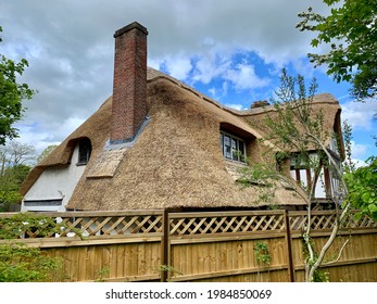 SONNING, ENGLAND - 24.05.2021. Fragment of medieval thatched half-timbered cottage with grass roof, brick chimney. English countryside. Wooden fence. Summertime. Selective focus
