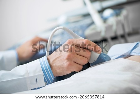 Sonogram procedure at modern hospital. Close-up doctors hand moving transducer on human belly. Professional clinical diagnostics and treatment. Ultrasound examination of human body internal organs