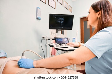 Sonographer doing ultrasound scanning procedure for young woman in modern clinic. Female patient lying on daybed during ultrasonography. Concept of healthcare, medical examination and sonography.