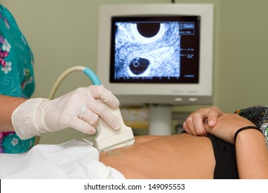 Sonographer technician holds an ultrasound transducer to diagnose the condition of a pregnant woman with a view of the woman's uterus on the computer screen.