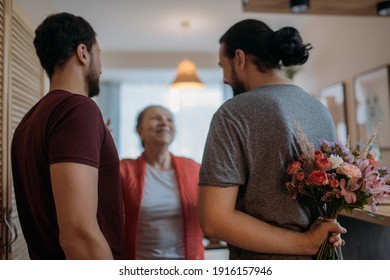 Sons congratulate mom on the holiday. Adult brothers give a bouquet of flowers to an elderly beautiful mother. Men visiting their beloved mother on a holiday