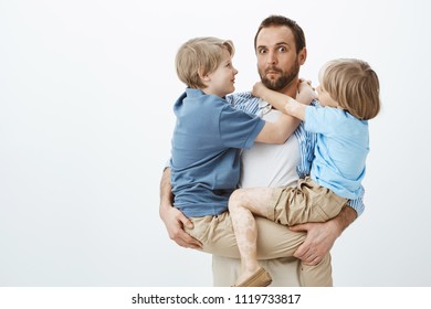 Sons Are Taking Advantage Of Loving And Caring Father. Portrait Of Clueless Funny European Dad Holding Children On Hands And Gazing Cluelessly At Camera, Boys Feeling Happy And Satisfied In Arms