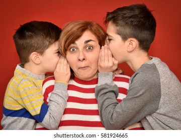 Sons whispering secret into ears of surprised mother