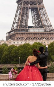 Soon to be married young couple is posing in front of the iconic Eiffel tower for their wedding photo album. Both bride and groom are formally dressed and cuddling. Groom is pointing the Eiffel tower.