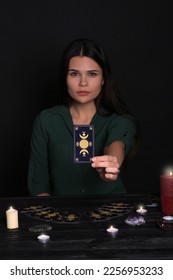 Soothsayer predicting future at table against black background, closeup. Focus on tarot card