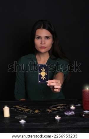 Soothsayer predicting future at table against black background, closeup. Focus on tarot card