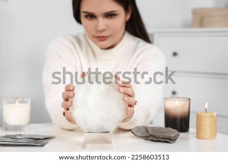Soothsayer predicting future at table in room, focus on crystal ball