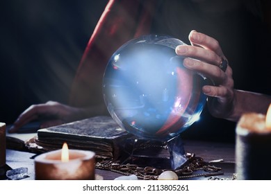 Soothsayer using crystal ball to predict future at table in darkness, closeup. Fortune telling