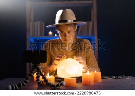 Soothsayer using crystal ball to predict future at table in darkness, online divination on smartphone webcam, closeup. Fortune telling concept