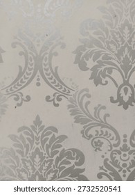 A sophisticated damask pattern wallpaper featuring elegant silver or light grey floral motifs on a neutral cream background. This classic Victorian-inspired design offers a luxurious texture, perfect 