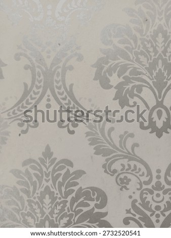 A sophisticated damask pattern wallpaper featuring elegant silver or light grey floral motifs on a neutral cream background. This classic Victorian-inspired design offers a luxurious texture, perfect 