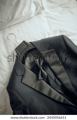 A sophisticated dark suit with a bow tie, neatly arranged on a white bed