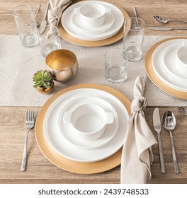 Sophisticated Table Setting with Gold-Rimmed White Porcelain Plates, Elegant Glassware, Stainless Steel Flatware, Linen Napkins with Knot Detailing, on a Natural Textured Table Runner, Top View. - Powered by Shutterstock