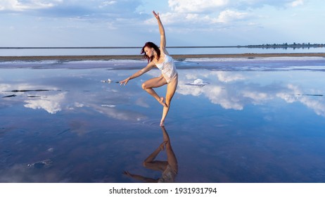 Sophisticated young girl dancer in a sexy costume on the mirror surface of a salt lake. dance in the clouds