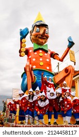 Sora, Italy - 28-02-2017: A Carnival Cart With A Huge Figure Of Pinocchio And A Group Of People Dressed As Pinocchio On A Platform Under It Rides Along The City Street During Fat Tuesday.