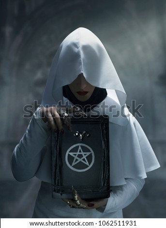 Sorceress preacher monk in white hooded cloak holding a spell magic book with pentagram symbol standing in the castle.