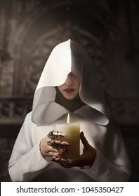 Sorceress In White Hooded Cloak Holding A Burning Candle Standing In The Castle.