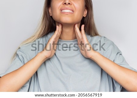 Sore throat. Cropped shot of a young caucasian blonde woman with a throat ache holding her neck isolated on a light gray background. Flu, cold, covid, tonsillitis, sars virus, inflamed tonsils