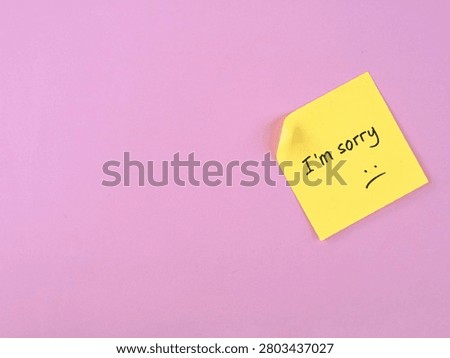 I'm sorry text handwritten with sad expression on yellow adhesive note on pink background. Represents themes of apology, regret, sadness, forgiveness, and emotional communication