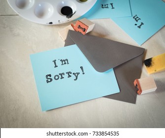 I'm Sorry Text on Handmade Note Card in Teal Color with Gray envelope still life in Flat Lay design and craft stamps and paint on a table. Overhead, above view horizontal with a dark, moody vignette. 库存照片