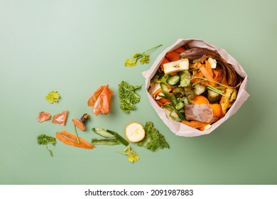 Sorted kitchen waste in paper eco bag on green background. Compost-container. Sustainable life style. Vegetable and fruit peels, scraps from food preparation collected in trash-pack for recycling - Shutterstock ID 2091987883