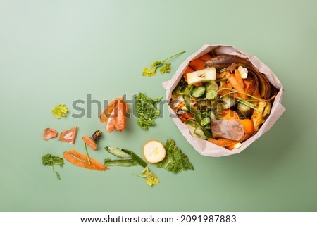 Sorted kitchen waste in paper eco bag on green background. Compost-container. Sustainable life style. Vegetable and fruit peels, scraps from food preparation collected in trash-pack for recycling