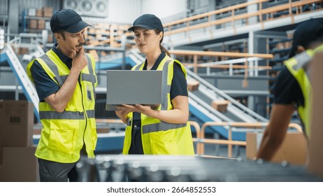 Sorting Center Facility: Supervisor and Manager Talk, Use Laptop. Logistics and Transportation Warehouse with Worker Loading Cardboard Boxes with Products on Conveyor Belt for Shipment to Clients - Powered by Shutterstock - Get 15% off with code: PIKWIZARD15