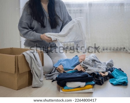 Sorting clothes from the wardrobe, unnecessary things are put in a cardboard box, things are donated. A woman is sorting through clothes.