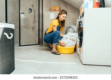 Sorting laundry before washing. A happy young housewife takes out or puts bed linen into the washing machine in a modern minimalist interior. - Powered by Shutterstock - Get 15% off with code: PIKWIZARD15