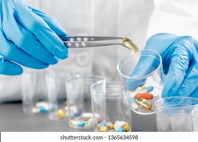 Sorting Medications. Doctor`s hand in blue gloves sorting with tweezers medication in glasses. Healthcare concept. - Powered by Shutterstock