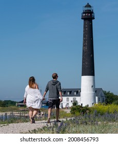 Sorvesaar,Estonia-06.21.2021: Lighthouse At The End Of Sorve Saar Peninsula. Tall Beacon Of Light For The Ship To Guide Them. Couple Walking Up To The Tall Tower Holding Hands. 