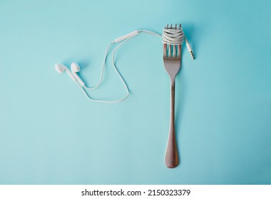 Soul Food. Studio Shot Of Earphones Wrapped Around A Fork Against A Blue Background.