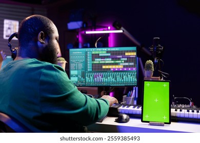 Sound engineer composing new tunes with daw interface, operating on greenscreen display. African american skilled musician mixing and mastering his recordings, stereo console and gear. - Powered by Shutterstock