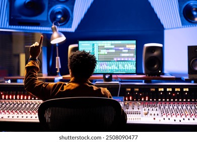 Sound engineer counting down to record singer in sound booth, doing a sign to let the artist know when to start the performance. Audio technician operating control room panel board desk.