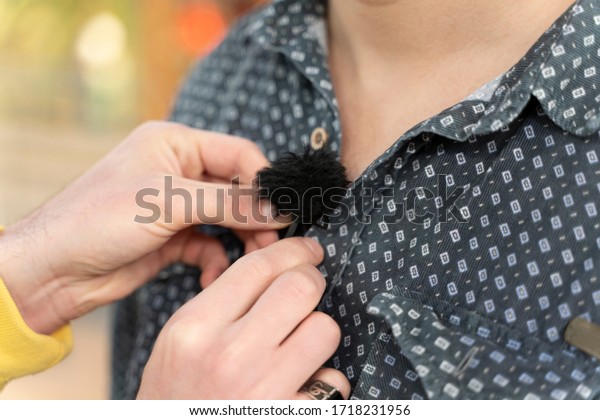 Sound engineer fastens lavalier microphone on\
actor\'s clothes for\
interview