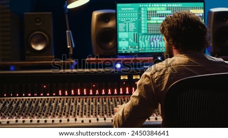 Sound engineer recording and editing tracks in control room, working with mixing console and technical gear in professional studio. Producer using audio software on pc to create. Camera A.