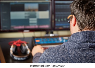 Sound engineer is sitting in front of a mixing desk and computer monitors and headphones.