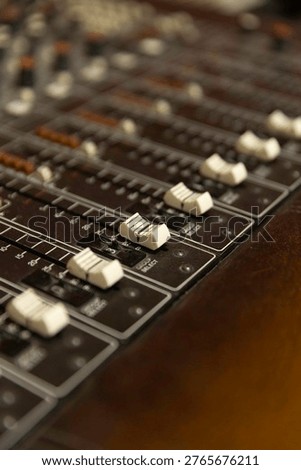 Sound engineers adjust faders and knobs on a mixing console in a recording studio. They work on sound levels while a band plays their music in the background.
