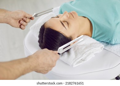 Sound healing specialist working with female patient. Man holding two metal tuning forks near young woman's head. Healer's hands close up. Holistic relaxation, music therapy, stress reduction concept - Powered by Shutterstock