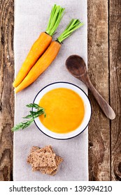 soup from carrots on bowl and ingredients with 2 carrots on rustic wooden table, bird`s eye view